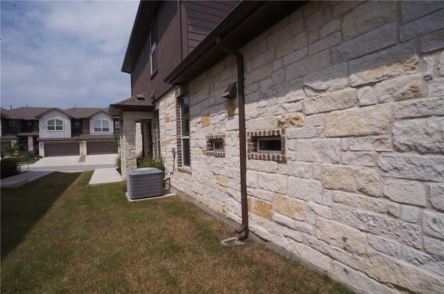 view of property exterior with driveway, stone siding, an attached garage, a yard, and central air condition unit