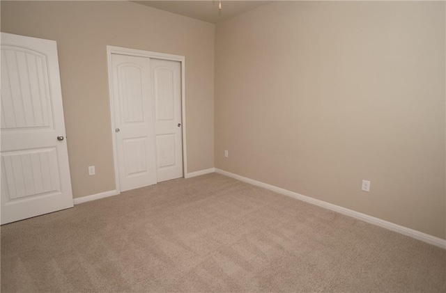 unfurnished bedroom featuring baseboards, a closet, and light colored carpet