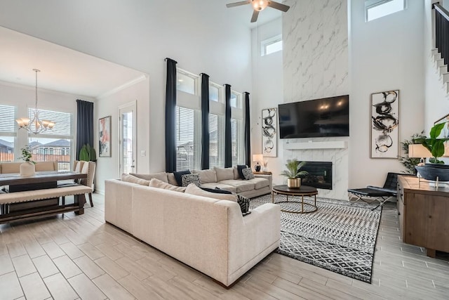 living room featuring a high end fireplace, a towering ceiling, ornamental molding, wood finish floors, and ceiling fan with notable chandelier