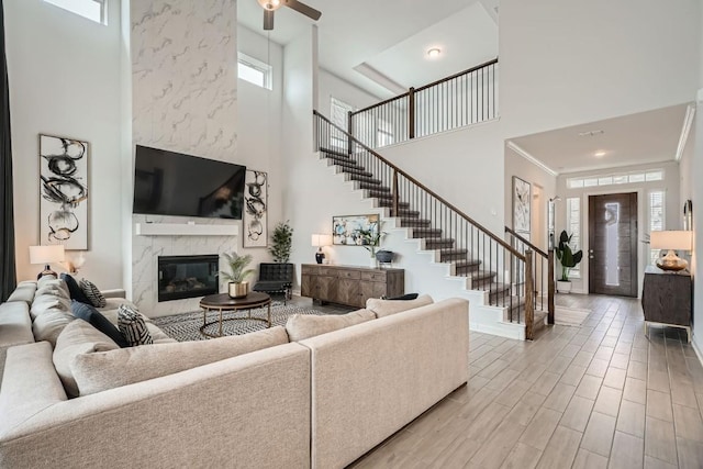 living room featuring a premium fireplace, stairway, a high ceiling, crown molding, and light wood-type flooring