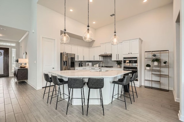 kitchen featuring white cabinets, light countertops, appliances with stainless steel finishes, decorative backsplash, and wood tiled floor