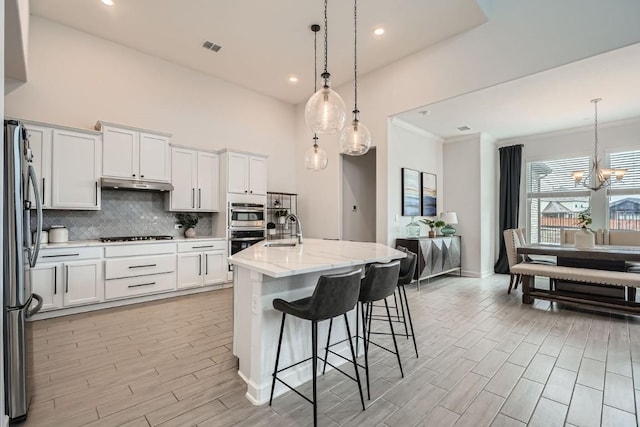 kitchen with white cabinets, under cabinet range hood, pendant lighting, and stainless steel appliances