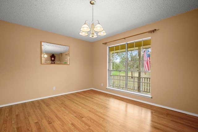 spare room with a textured ceiling, an inviting chandelier, and wood finished floors