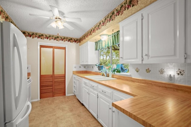 kitchen with a textured ceiling, white appliances, a sink, and white cabinetry