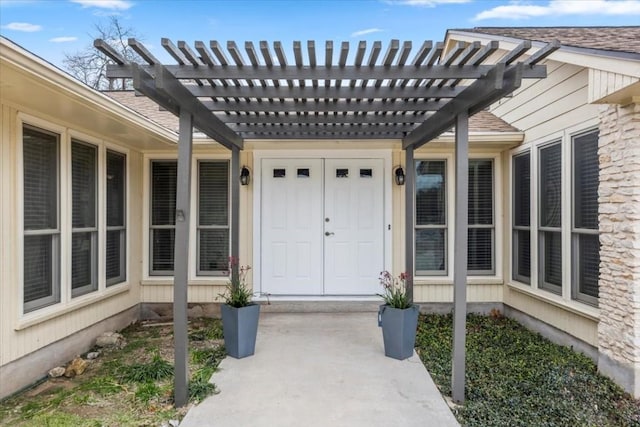 doorway to property featuring a shingled roof and a pergola