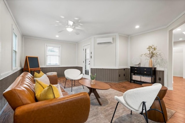 living room featuring light wood-type flooring, ornamental molding, a wall mounted air conditioner, and a ceiling fan