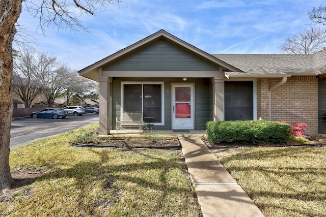 view of front facade with a shingled roof, a front yard, and brick siding