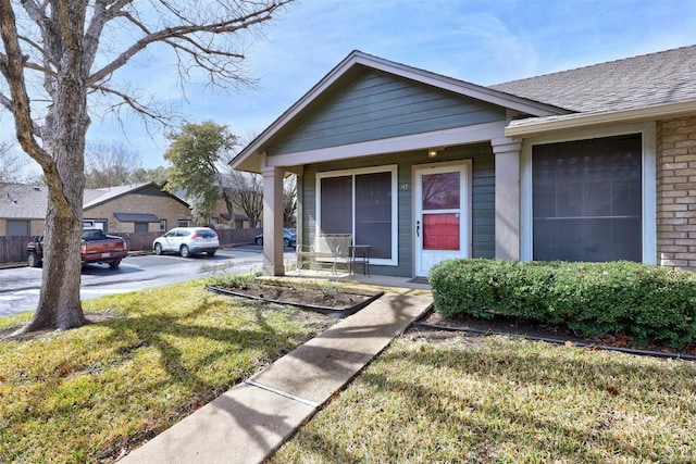 view of front of home featuring covered porch, brick siding, roof with shingles, and a front yard