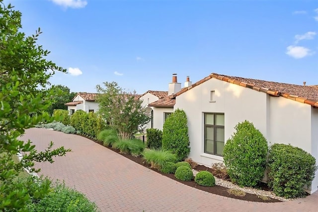 view of side of property featuring a chimney, a tile roof, and stucco siding