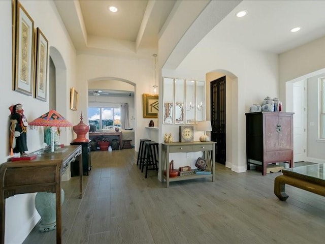 corridor with arched walkways, recessed lighting, wood finished floors, baseboards, and a tray ceiling