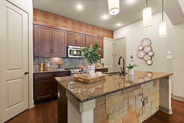 kitchen with dark stone counters, dark wood-style floors, appliances with stainless steel finishes, decorative light fixtures, and a sink