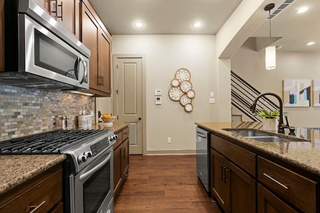 kitchen featuring stainless steel appliances, a sink, hanging light fixtures, backsplash, and light stone countertops