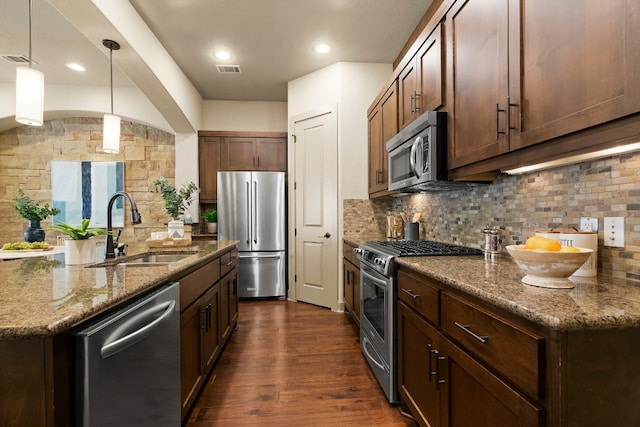 kitchen featuring stainless steel appliances, a sink, backsplash, dark stone countertops, and pendant lighting