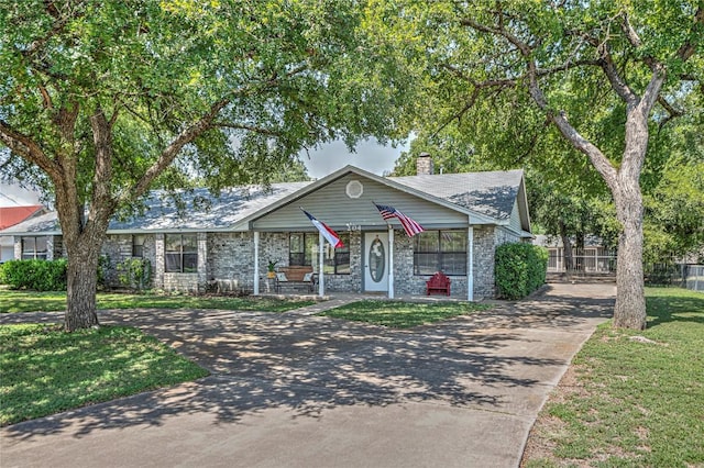 view of front facade with covered porch, driveway, stone siding, a front lawn, and a chimney