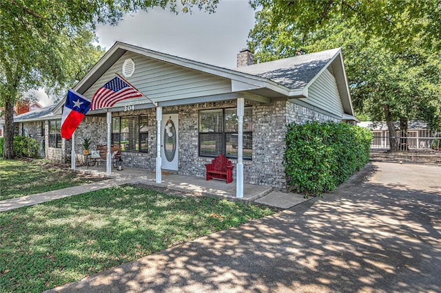 view of front facade featuring covered porch, a chimney, fence, and a front lawn