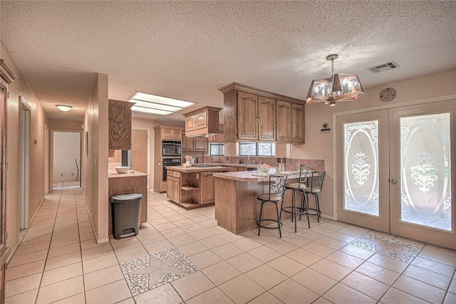 kitchen featuring a peninsula, visible vents, light countertops, black appliances, and a kitchen bar