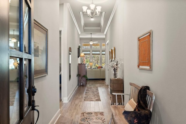 hall featuring a notable chandelier, a raised ceiling, ornamental molding, wood finished floors, and baseboards