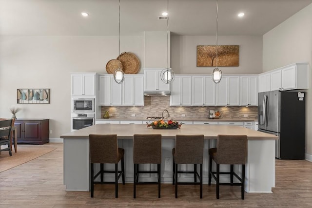 kitchen featuring hanging light fixtures, appliances with stainless steel finishes, light countertops, and a center island with sink