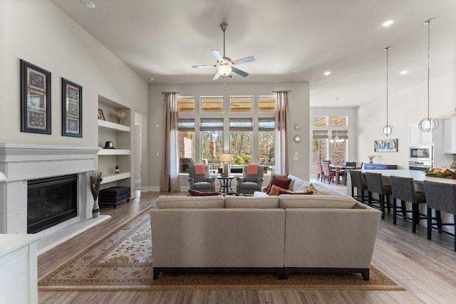 living room featuring built in shelves, a glass covered fireplace, light wood-style flooring, and baseboards