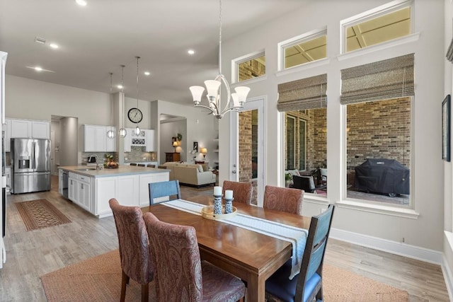 dining room with recessed lighting, a high ceiling, an inviting chandelier, light wood-style floors, and baseboards