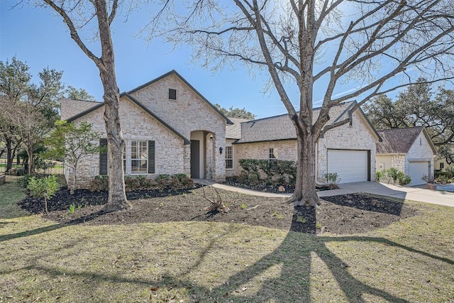 french country home featuring a garage, driveway, stone siding, and a front yard