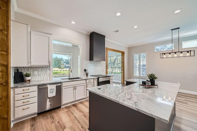 kitchen featuring stainless steel appliances, ornamental molding, white cabinets, a sink, and wall chimney exhaust hood