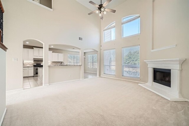 1003 Preserve Pl, Round Rock, TX 78665 - unfurnished living room featuring a towering ceiling, light colored carpet, a ceiling fan, arched walkways, and a fireplace with raised hearth