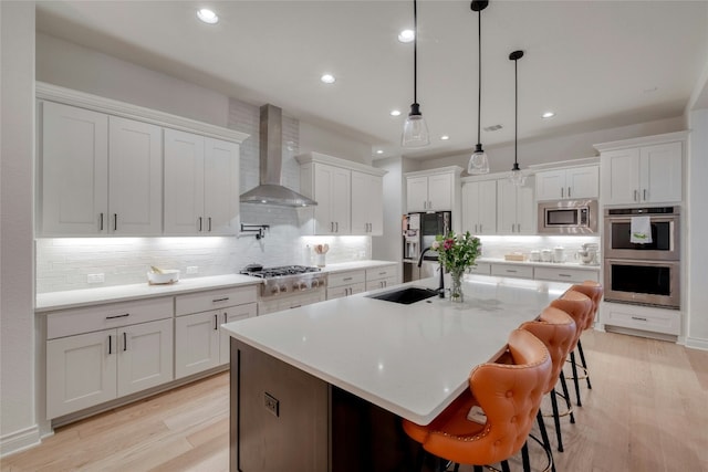 521 Wonderstruck, Liberty Hill, TX 78642 - kitchen featuring wall chimney exhaust hood, appliances with stainless steel finishes, light wood finished floors, white cabinetry, and tasteful backsplash
