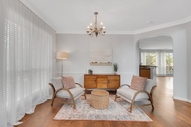 sitting room featuring an inviting chandelier, light wood-style flooring, arched walkways, and ornamental molding