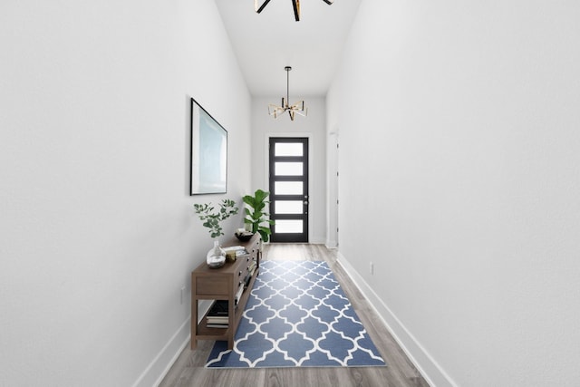 doorway featuring baseboards, wood finished floors, and a notable chandelier