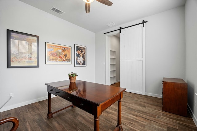 office space featuring visible vents, a barn door, dark wood-type flooring, a ceiling fan, and baseboards