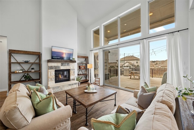 living room with high vaulted ceiling, a stone fireplace, and wood finished floors