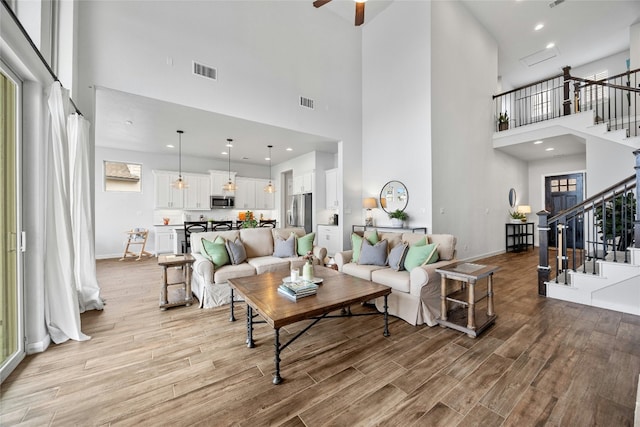 living room with light wood-type flooring, visible vents, and stairway