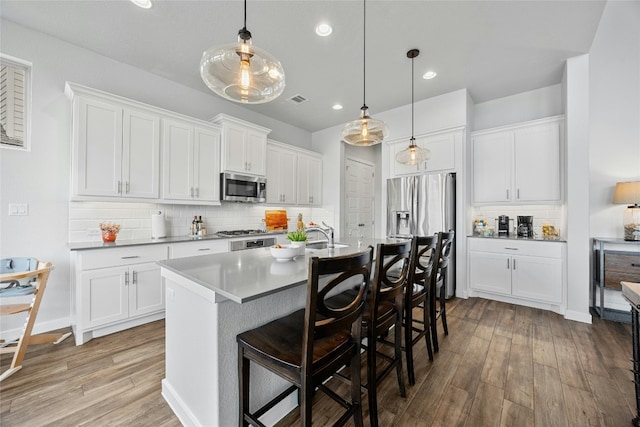 kitchen featuring appliances with stainless steel finishes, a breakfast bar, decorative light fixtures, light wood-style floors, and white cabinetry