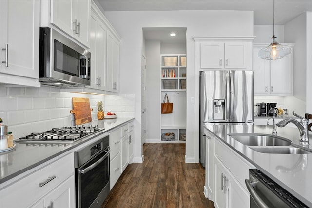 kitchen featuring white cabinetry, stainless steel appliances, a sink, and decorative light fixtures