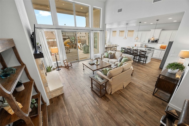 living area featuring dark wood-type flooring, recessed lighting, visible vents, and a towering ceiling