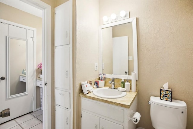 bathroom featuring toilet, a textured wall, vanity, and tile patterned floors