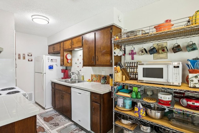 kitchen featuring tasteful backsplash, a sink, a textured ceiling, dark brown cabinetry, and white appliances