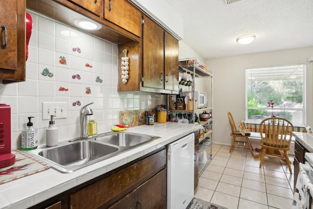 kitchen with light tile patterned floors, tile counters, decorative backsplash, white dishwasher, and a sink