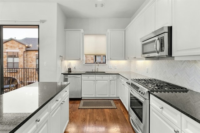 kitchen with visible vents, dark stone countertops, stainless steel appliances, white cabinetry, and a sink