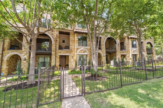 view of front facade with a fenced front yard, stone siding, a front yard, and a balcony