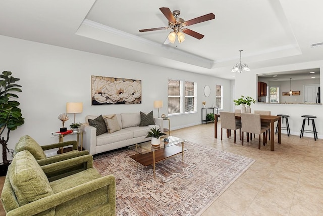 living room featuring plenty of natural light, baseboards, a raised ceiling, and ceiling fan with notable chandelier