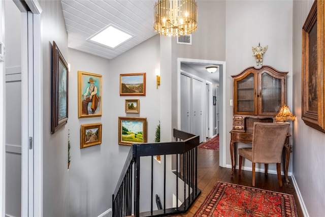 hall featuring lofted ceiling, visible vents, an upstairs landing, wood finished floors, and baseboards