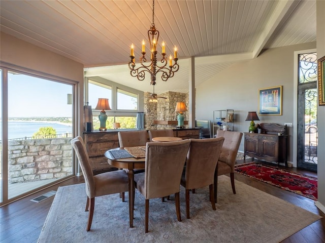 dining area with visible vents, wood-type flooring, vaulted ceiling with beams, an inviting chandelier, and a water view