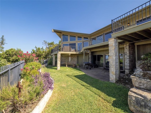 exterior space featuring stone siding, a fenced backyard, a yard, and a balcony