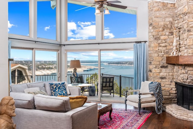 living room with ceiling fan, a stone fireplace, wood finished floors, and a healthy amount of sunlight