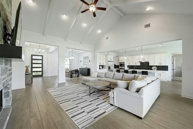 living room with high vaulted ceiling, a fireplace, light wood-style flooring, and beamed ceiling