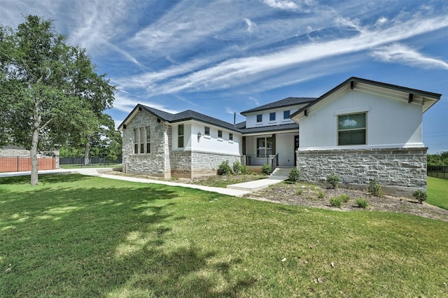 view of front of home with covered porch, stone siding, a front lawn, and fence