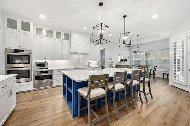 kitchen with a center island with sink, a breakfast bar area, hanging light fixtures, double oven, and glass insert cabinets