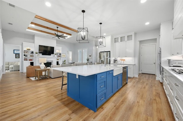 kitchen with a center island with sink, open floor plan, blue cabinets, light countertops, and white cabinetry